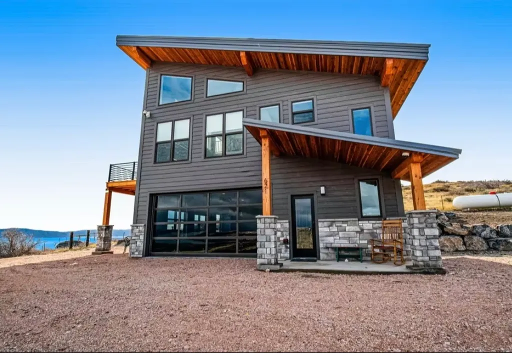 A finished modern home with a glass garage door, cedar soffits and stone-wrapped porch posts