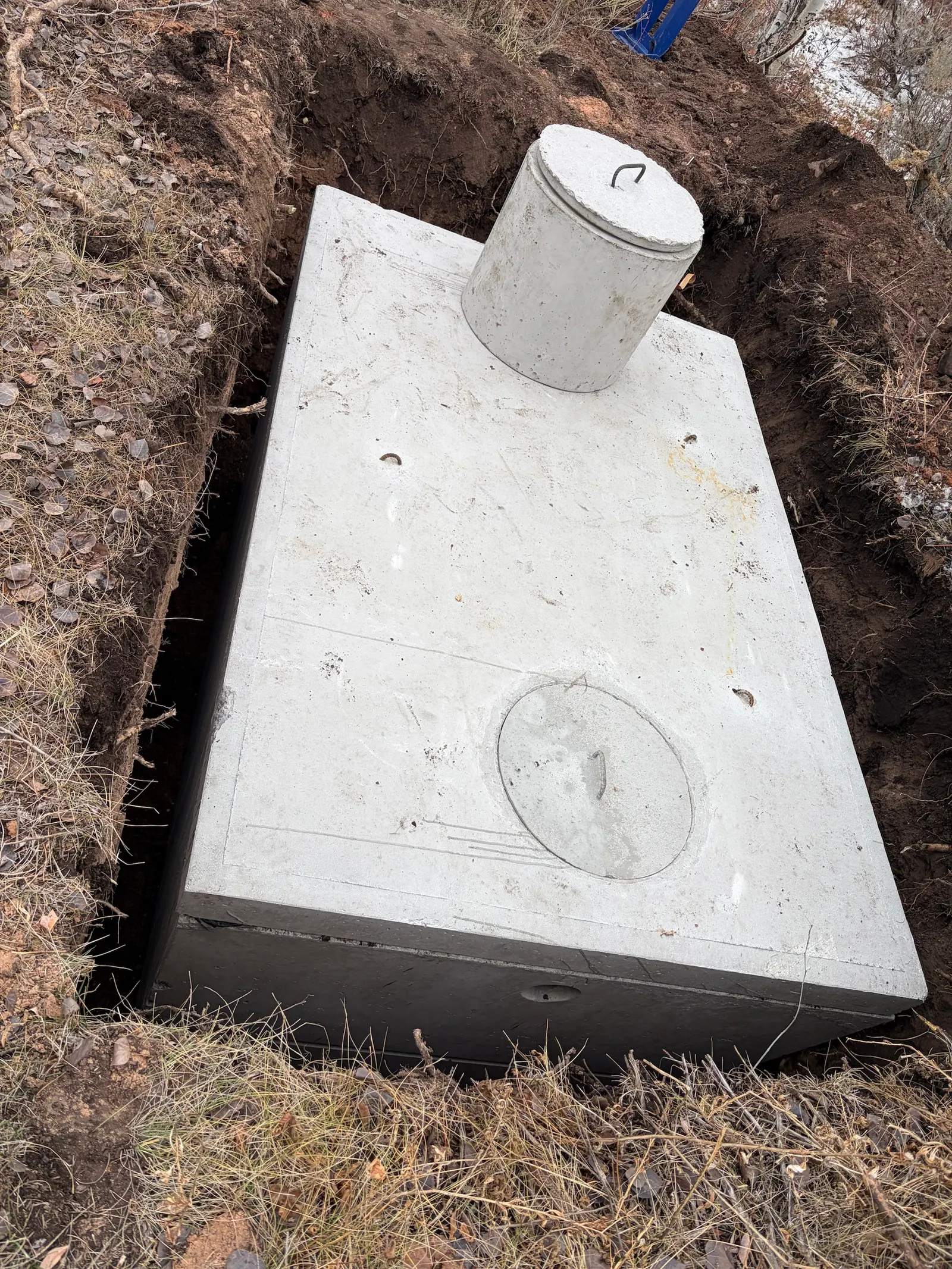 A new concrete septic tank with a riser and lid, set level in a freshly dug pit