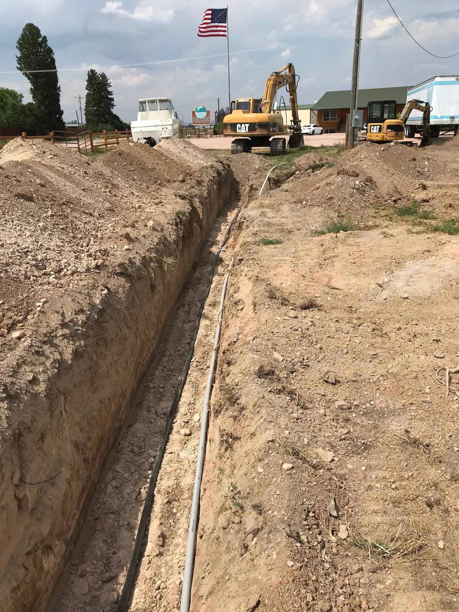 A long, deep trench with utility lines laid in the bottom, with excavators parked beyond it